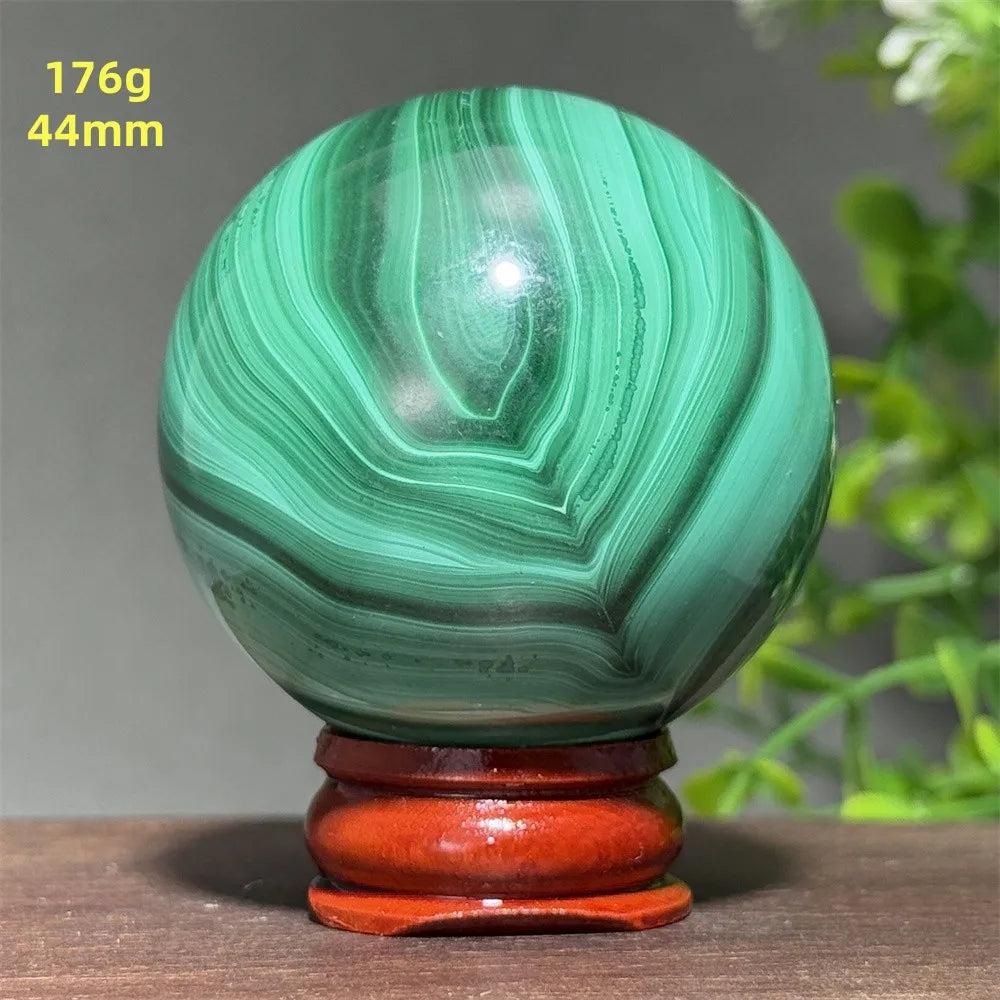 Polished 44mm Malachite crystal sphere featuring deep green banded patterns on a wooden display base for healing energy.