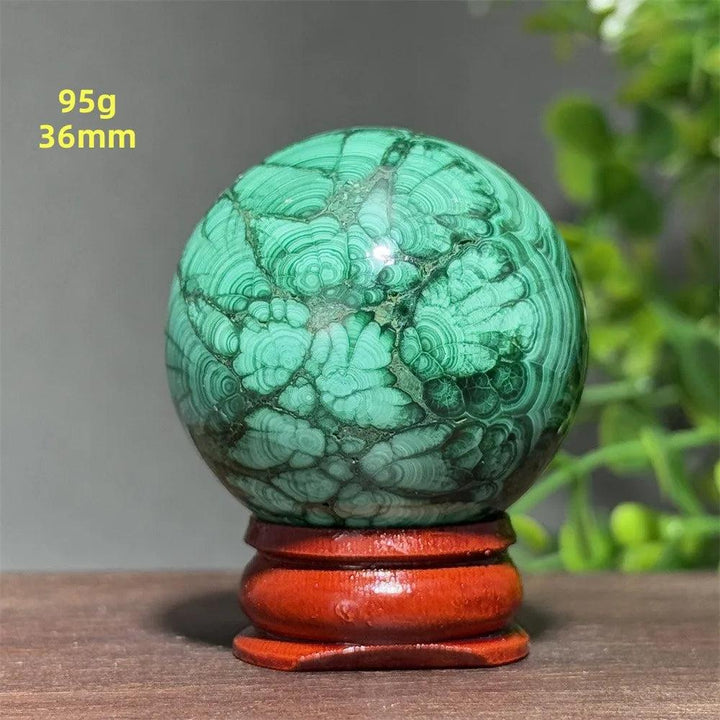 Polished 36mm malachite crystal sphere featuring deep green banded patterns on a wooden display base for transformation.