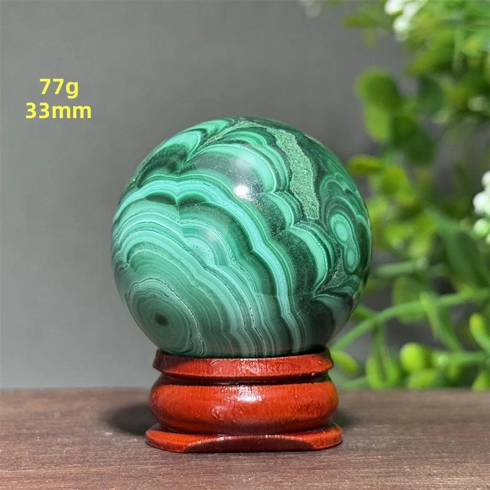 Polished 33mm Malachite crystal sphere featuring deep green banded patterns on a wooden display base for transformation.