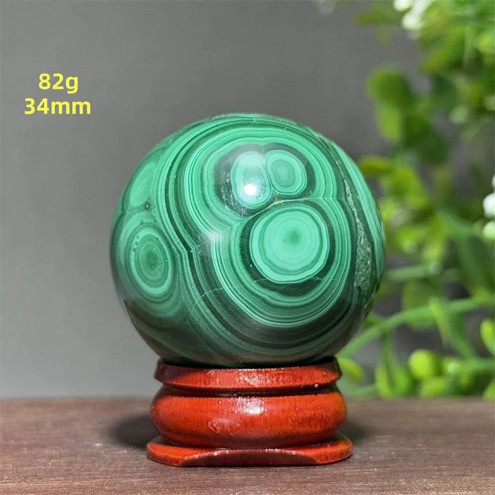 34mm polished Malachite crystal sphere with deep green banded patterns on a wooden display base for healing energy.