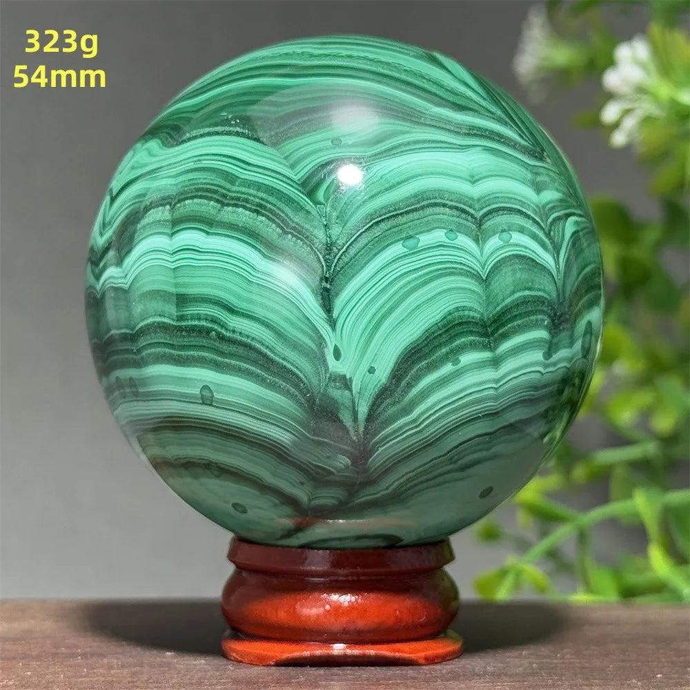 Polished 54mm Malachite crystal sphere featuring deep green banded patterns for transformation on a wooden display base.