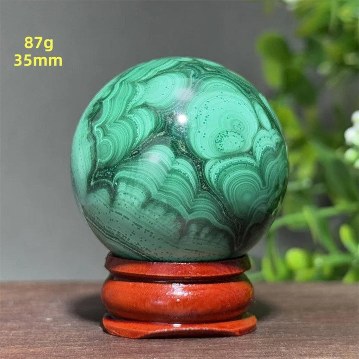 AAAAA Malachite crystal sphere featuring deep green banded patterns on a wooden display base for healing and growth.