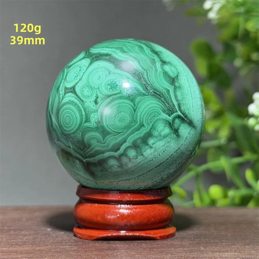 Polished 39mm Malachite crystal sphere featuring deep green concentric banding on a wooden display base for transformation.