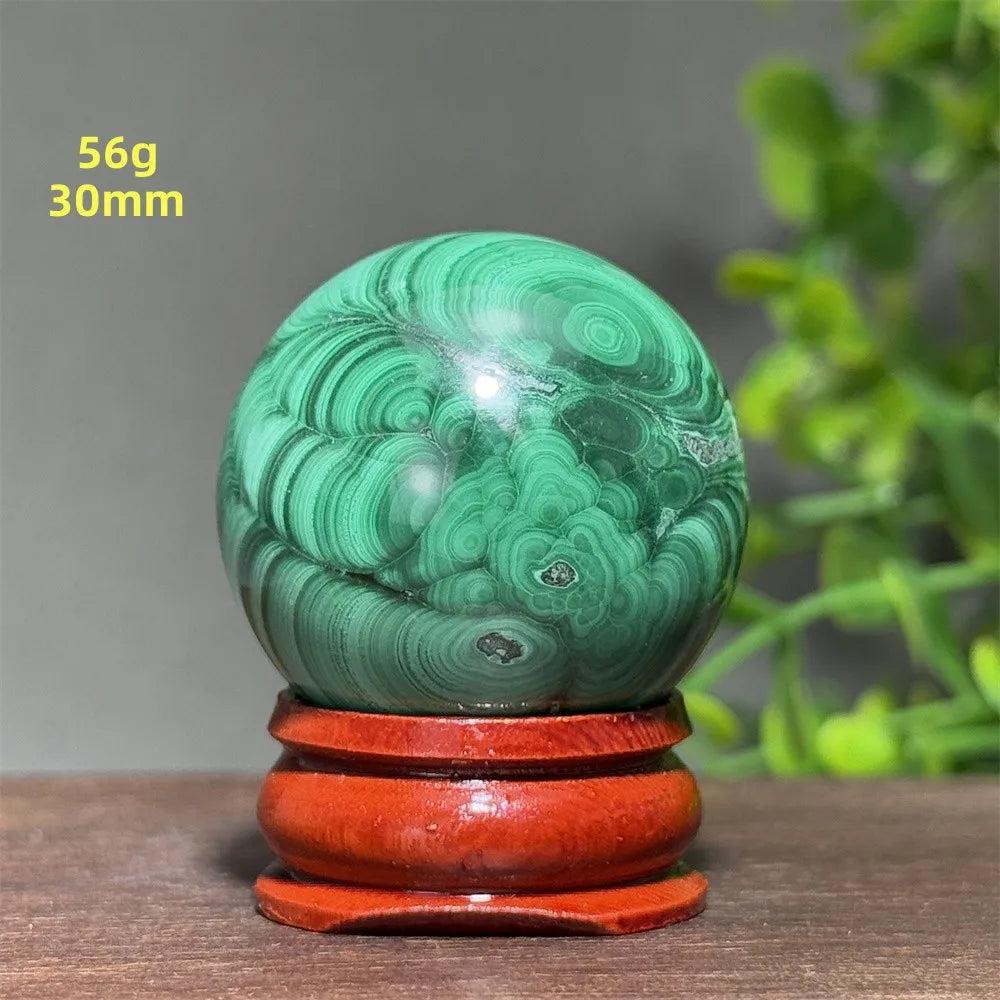 Polished 30mm Malachite crystal sphere with deep green banded patterns on a wooden display base for healing energy.