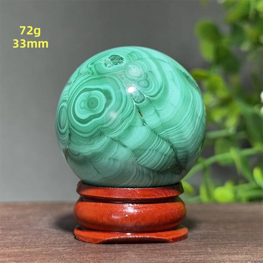 Polished 33mm Malachite crystal sphere featuring deep green banded patterns on a wooden display base for healing energy.