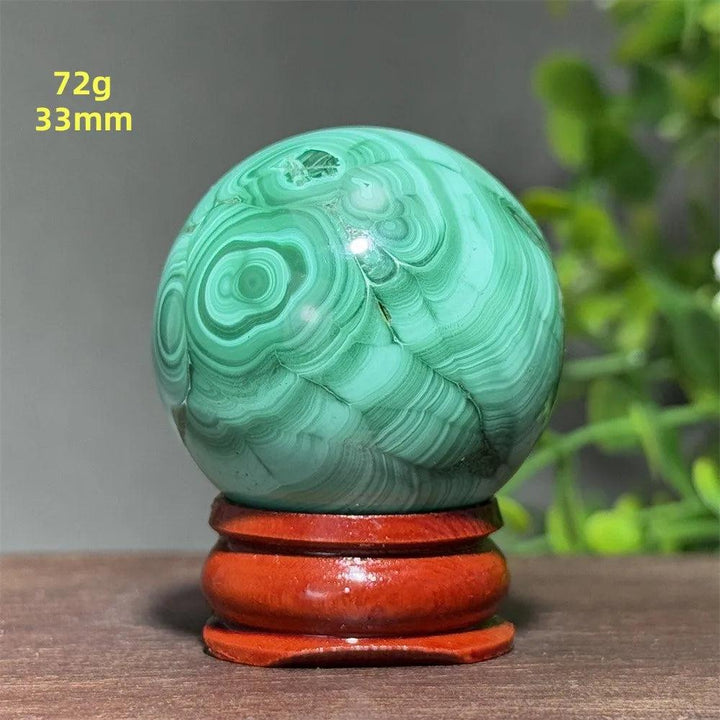 Polished 33mm Malachite crystal sphere featuring deep green banded patterns on a wooden display base for healing energy.
