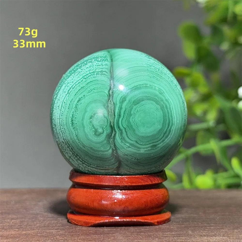 Polished 33mm Malachite crystal sphere featuring deep green concentric banding on a wooden display base for healing.
