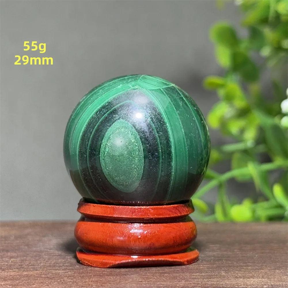 Polished 29mm Malachite crystal sphere featuring deep green banded patterns on a wooden display base for healing.