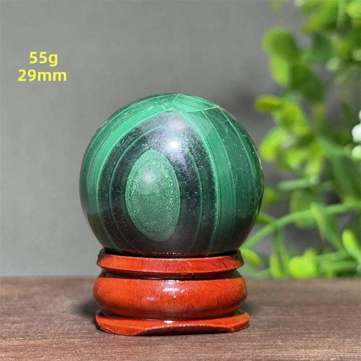 Polished 29mm Malachite crystal sphere featuring deep green banded patterns on a wooden display base for healing.
