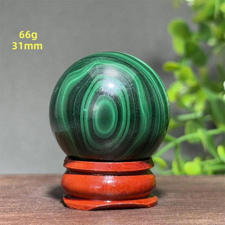 AAAAA grade Malachite crystal sphere with deep green banded patterns on a wooden display base for healing and growth.
