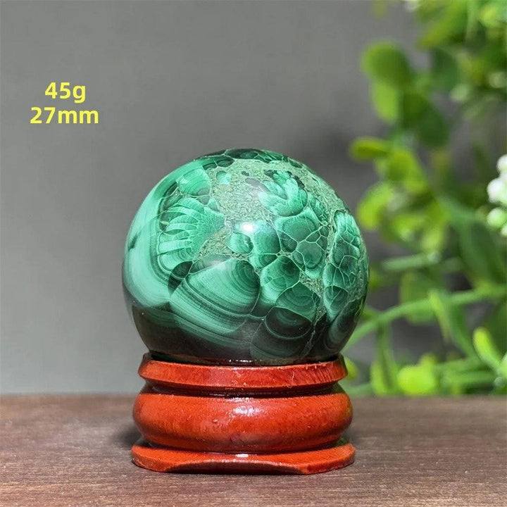 Polished 27mm Malachite crystal sphere featuring deep green banded patterns on a wooden display base for healing.