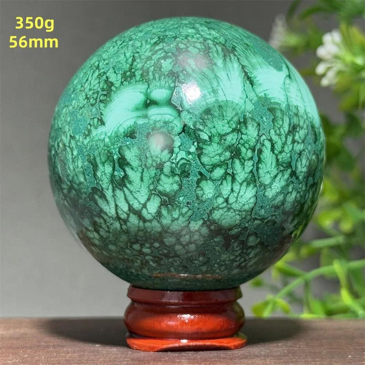 56mm Malachite Crystal Sphere with deep green banded patterns on a wooden display base for healing and transformation.
