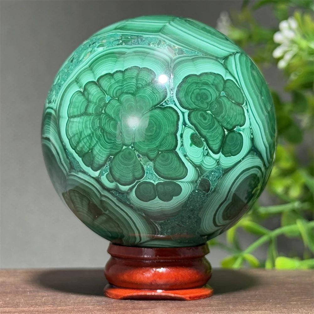 AAAAA grade Malachite crystal sphere featuring deep green concentric banding on a wooden display base for transformation.