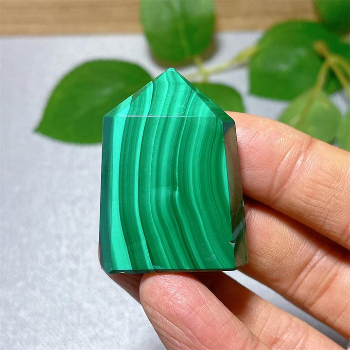 Handheld Malachite Crystal Tower with vibrant green banded patterns, perfect for heart chakra healing and transformation.