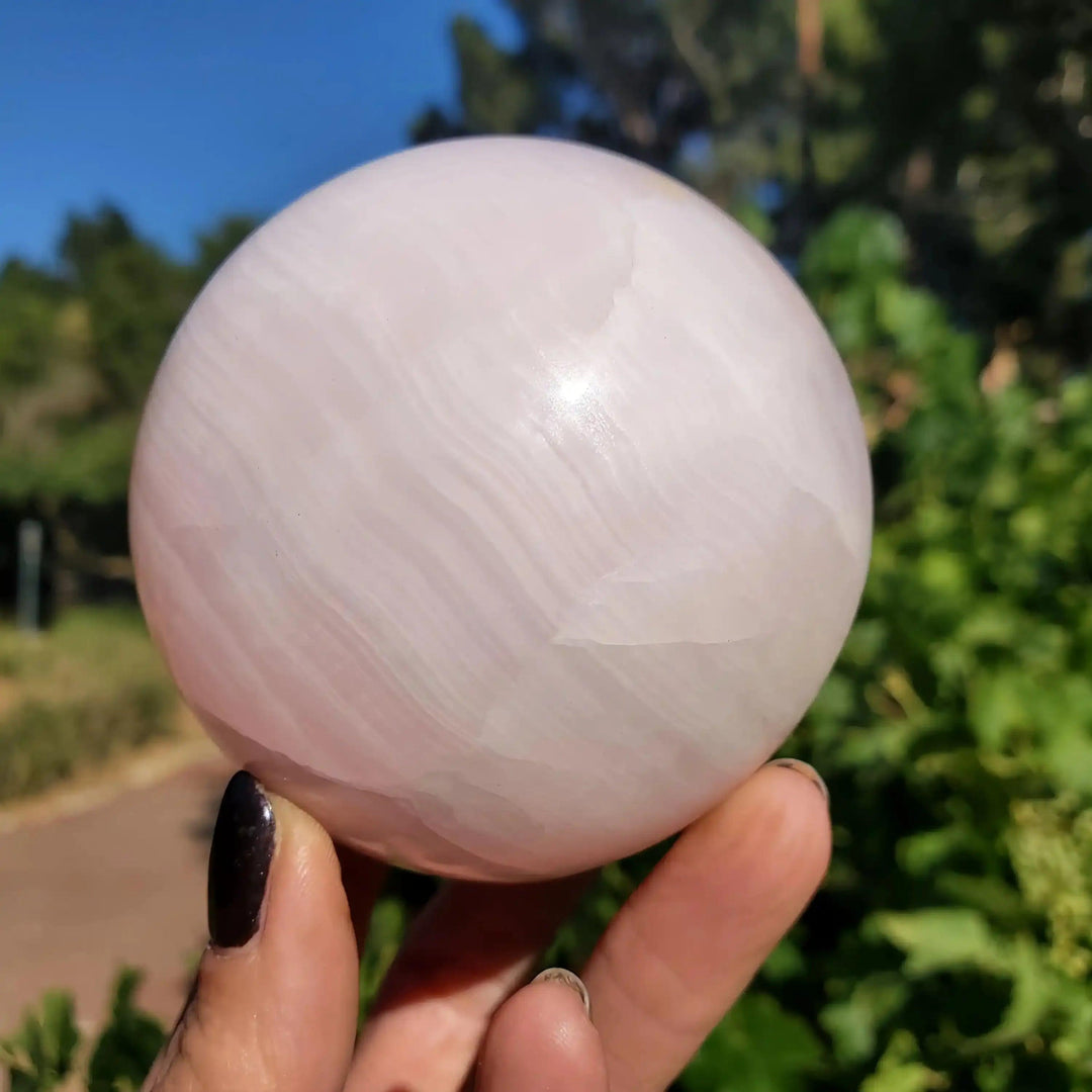 Hand-polished Mangano Calcite sphere featuring soft pastel pink hues and creamy white banding for Heart chakra healing.