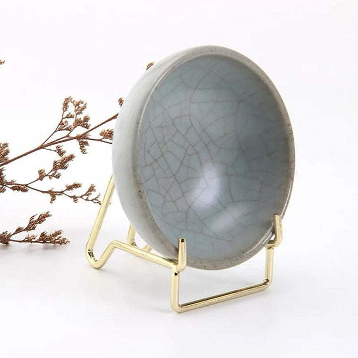 Gold metal arm easel displaying a crackled gray ceramic bowl, ideal for crystals or geodes.