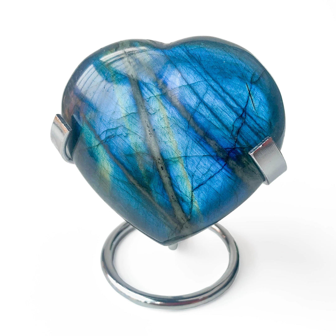 Heart-shaped labradorite crystal sphere on a silver metal display stand, showcasing its iridescent blue and green hues.