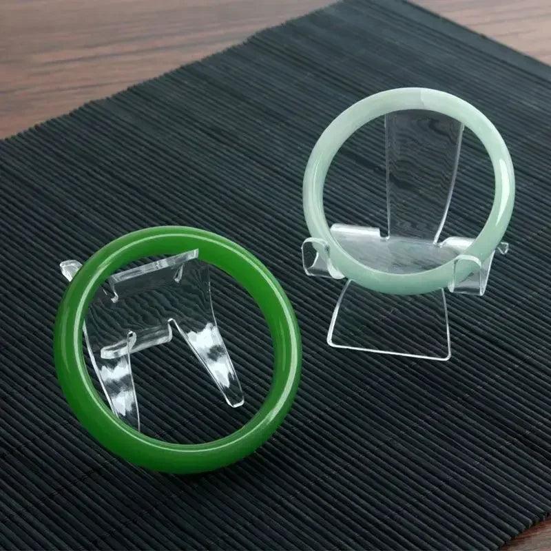 Two clear acrylic easel stands displaying a vibrant green jade bangle and a pale green jade bangle.