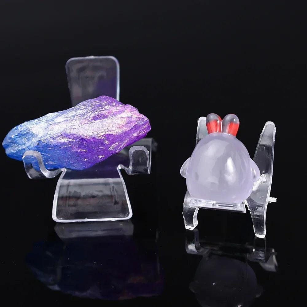 Clear acrylic easel stands displaying a raw blue-purple aura quartz and a lavender rose quartz crab carving.