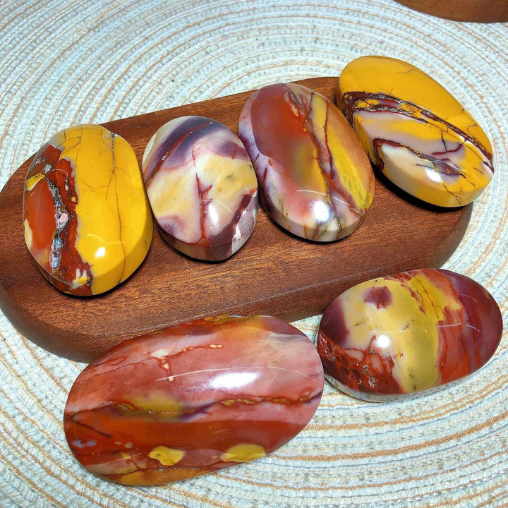 Smooth, polished Mookaite Jasper palm stones in vibrant red, yellow, and mauve swirls for grounding and vitality.