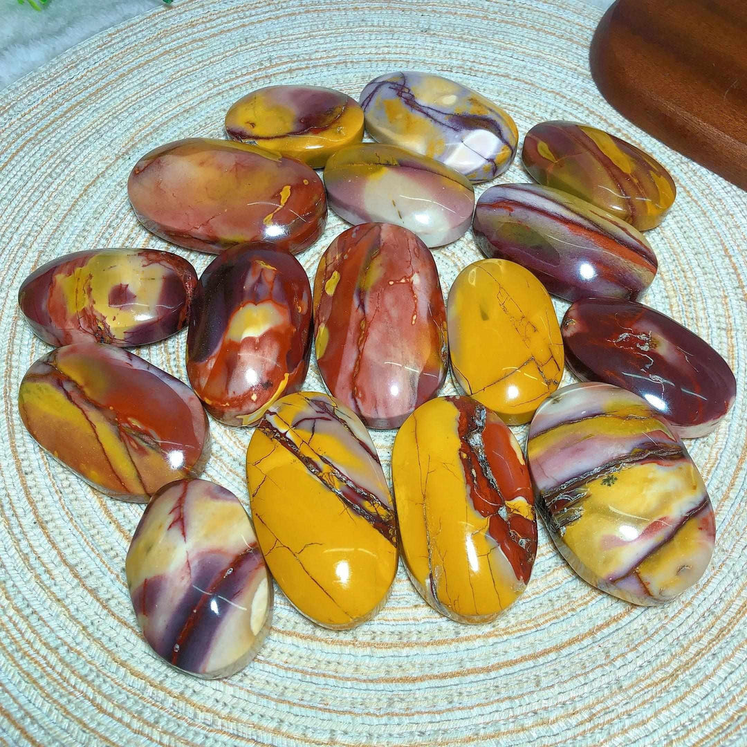 Smooth, polished Mookaite Jasper palm stones featuring vibrant swirls of red, mustard yellow, cream, and mauve patterns.