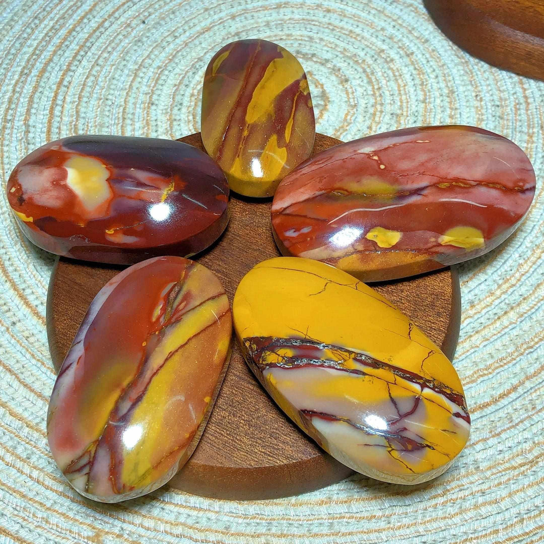 Smooth Mookaite Jasper palm stones featuring vibrant swirls of red, yellow, and mauve for grounding and vitality.