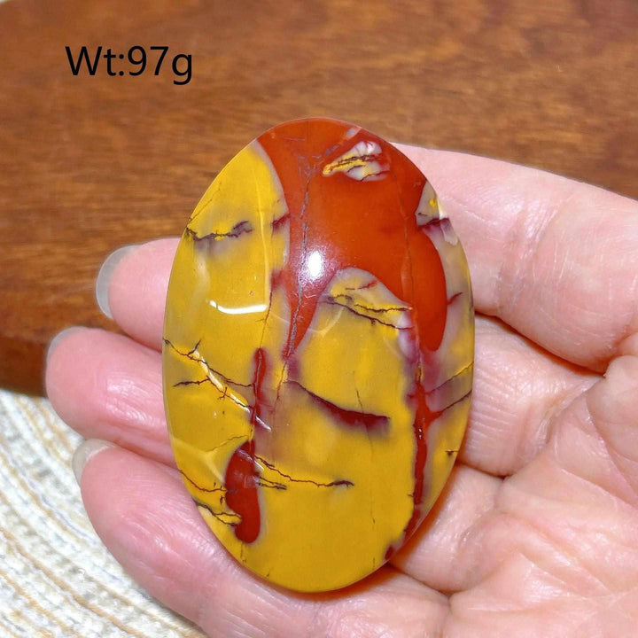 Smooth, polished Mookaite Jasper palm stone featuring vibrant red and mustard yellow swirls for grounding energy.