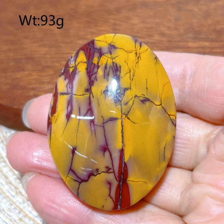 Smooth, polished Mookaite Jasper palm stone featuring vibrant red and mustard yellow swirls for grounding and vitality.