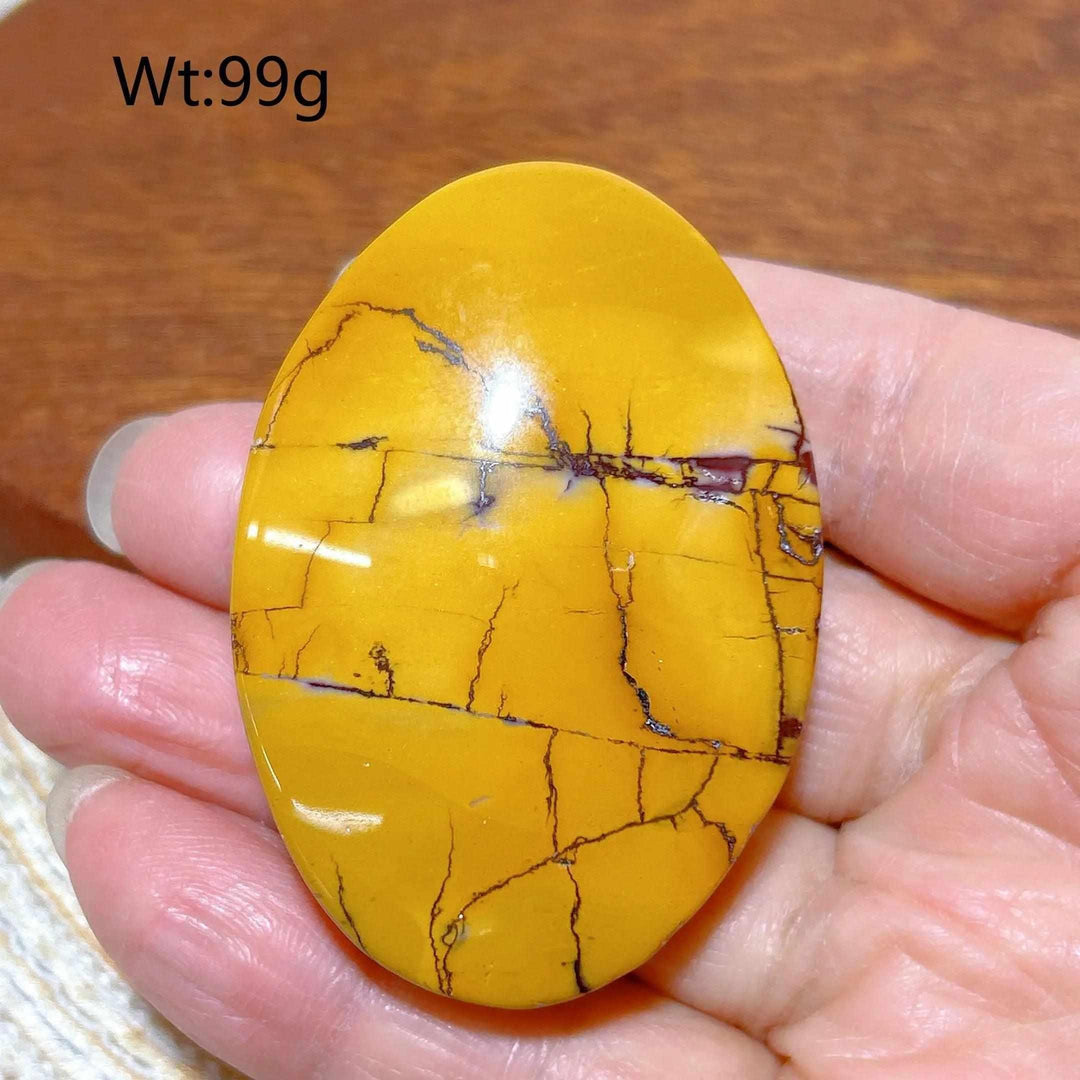 Smooth mustard yellow Mookaite Jasper palm stone with grounding red veins, held in hand for vitality and energy.