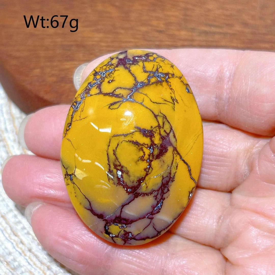 Smooth, polished Mookaite Jasper palm stone featuring vibrant mustard yellow and deep red swirls for grounding energy.
