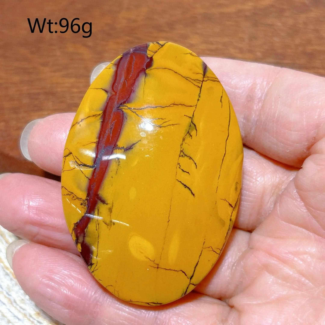 Smooth Mookaite Jasper palm stone featuring vibrant mustard yellow and deep red swirls for grounding energy.