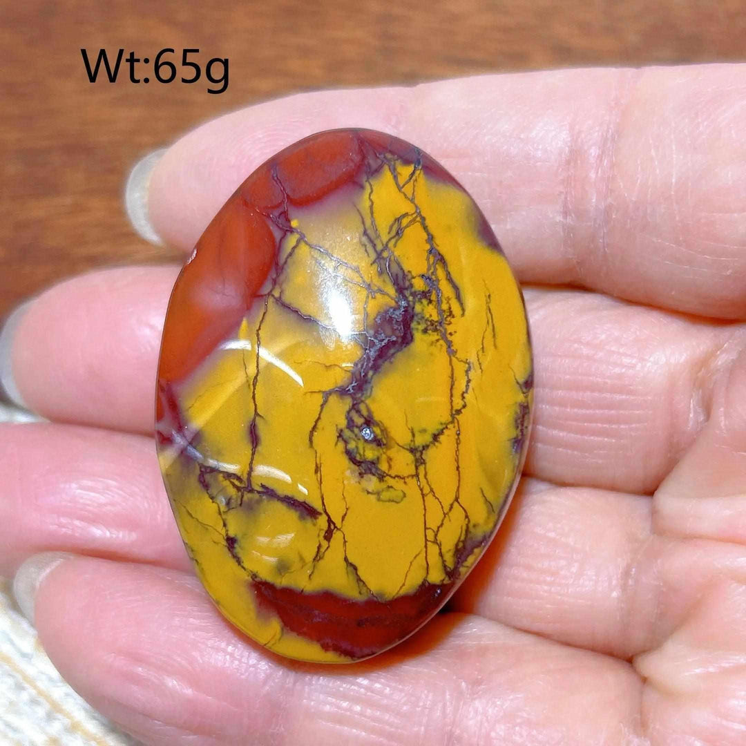 Smooth Mookaite Jasper palm stone featuring vibrant red and mustard yellow swirls for grounding and vitality.