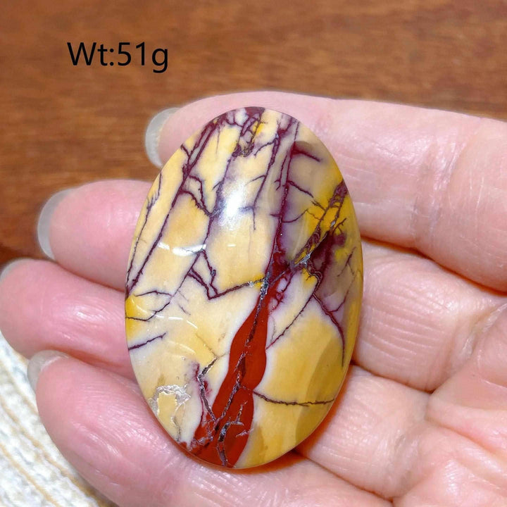 Smooth, polished Mookaite Jasper palm stone featuring vibrant red, yellow, and cream swirls for grounding energy.