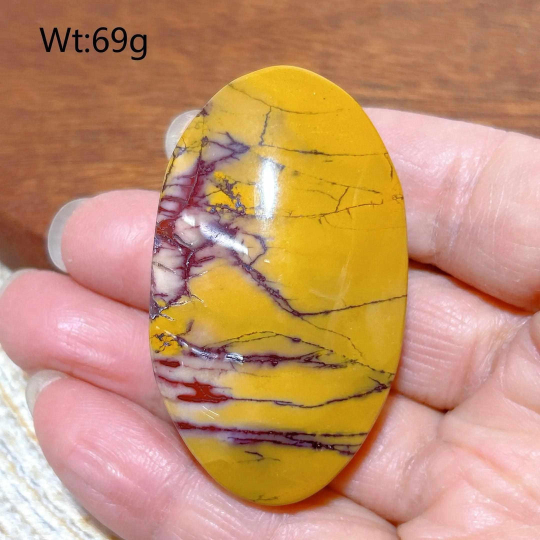 Smooth, oval Mookaite Jasper palm stone featuring vibrant mustard yellow, red, and cream swirls for grounding energy.