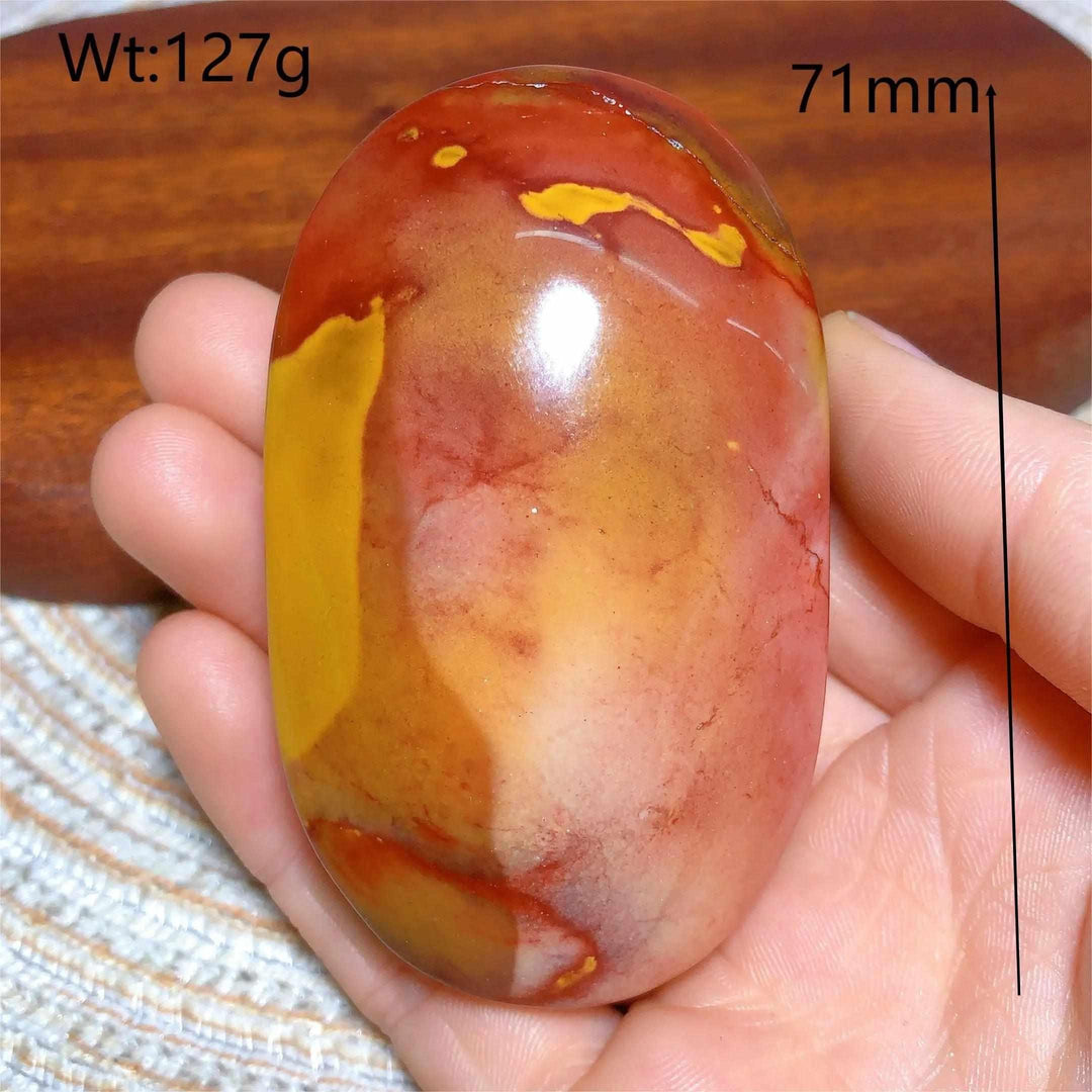 Smooth, polished Mookaite Jasper palm stone featuring vibrant red, yellow, and cream swirls for grounding and vitality.