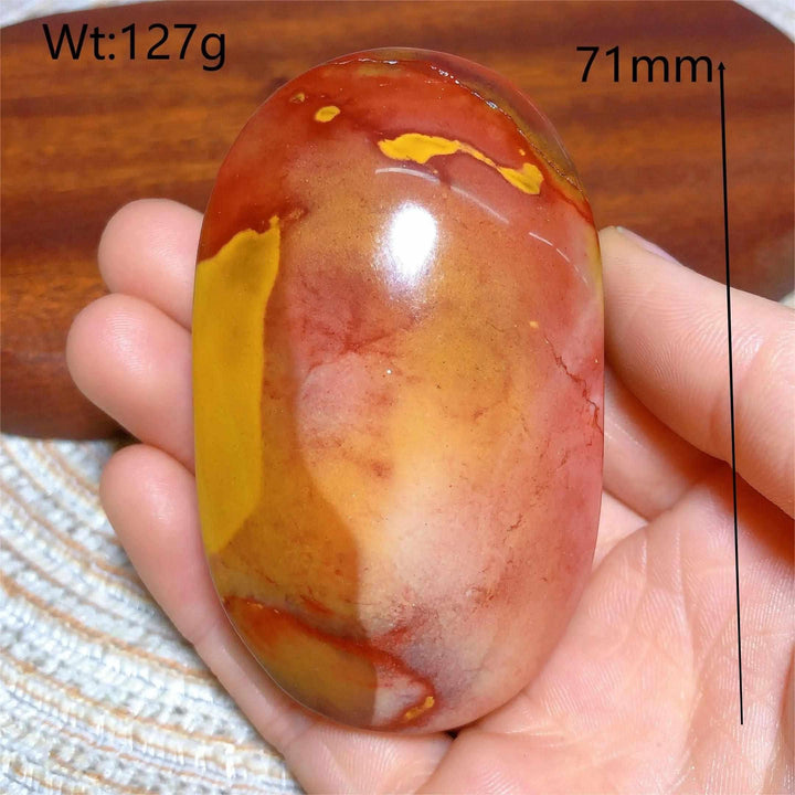 Smooth, polished Mookaite Jasper palm stone featuring vibrant red, yellow, and cream swirls for grounding and vitality.