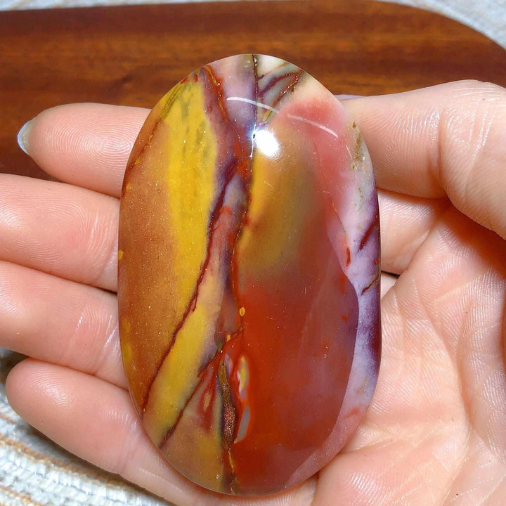 Smooth Mookaite Jasper palm stone featuring vibrant red, yellow, and mauve swirls for grounding and vitality.
