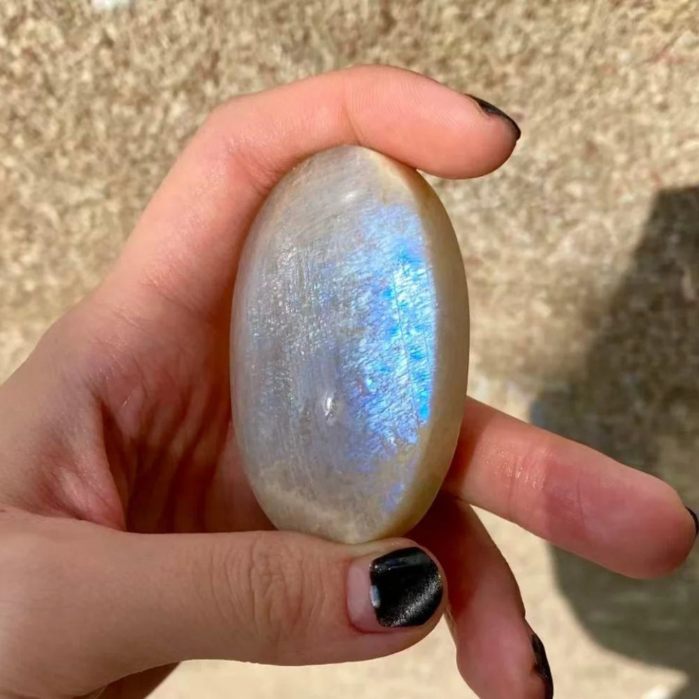 Hand-polished white moonstone palm stone featuring a vibrant blue flash, perfect for meditation and crystal healing.