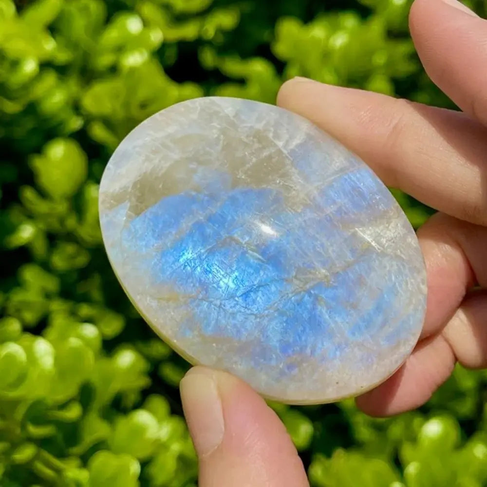Polished white moonstone palm stone with vibrant blue flash, perfect for healing, meditation, and crystal jewelry making.