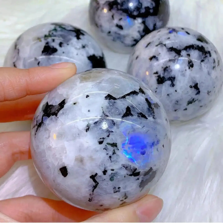 Polished moonstone sphere with black inclusions and glowing blue flash, perfect for crystal healing and home decor.