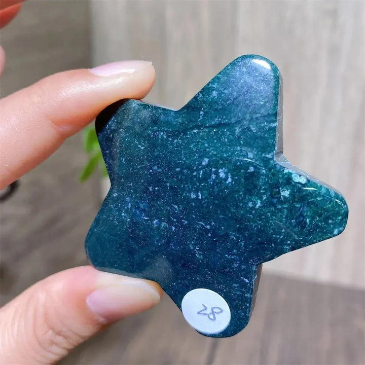 Hand-carved moss agate star crystal carving, deep green with natural inclusions, held for scale.