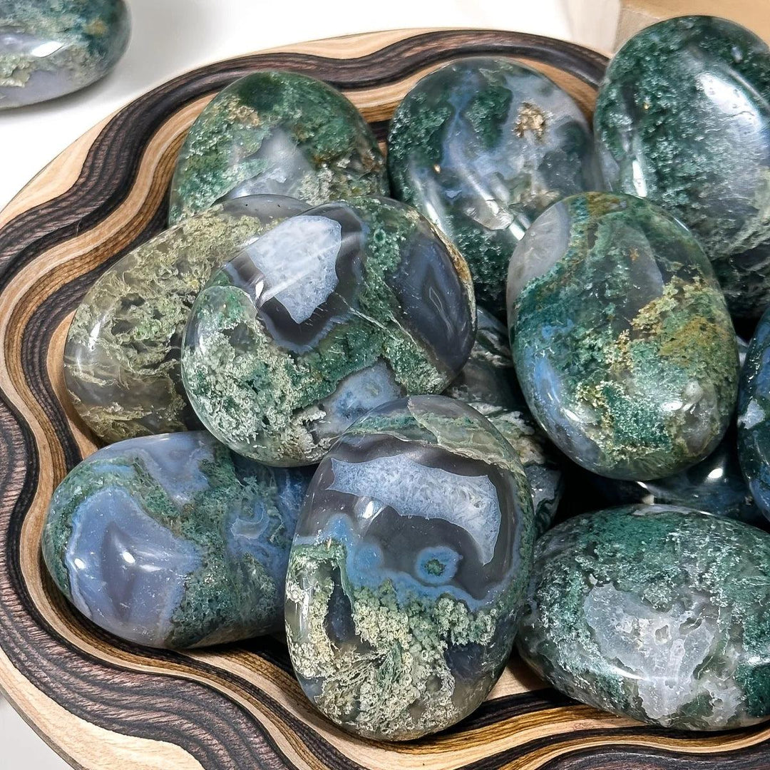 Polished Moss Agate palm stones with green moss-like inclusions in a wooden bowl for grounding and heart chakra healing.