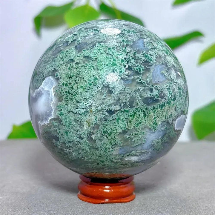 Moss Agate Sphere 78mm: Hand-polished, translucent green and white chalcedony with dendritic inclusions on a wooden stand.