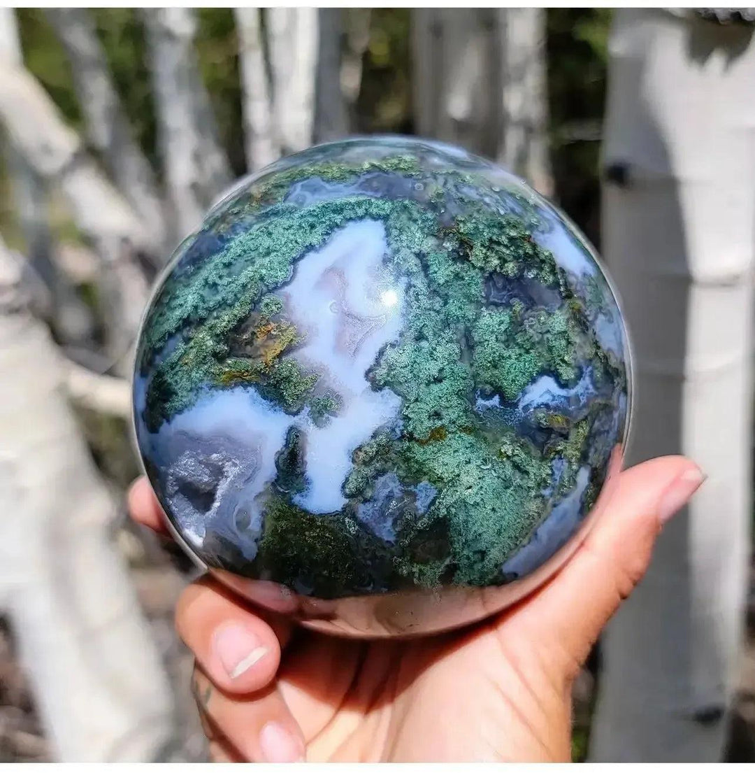 Hand holding a polished Moss Agate Crystal Sphere with green moss-like inclusions and white quartz, from Crystal Destiny.