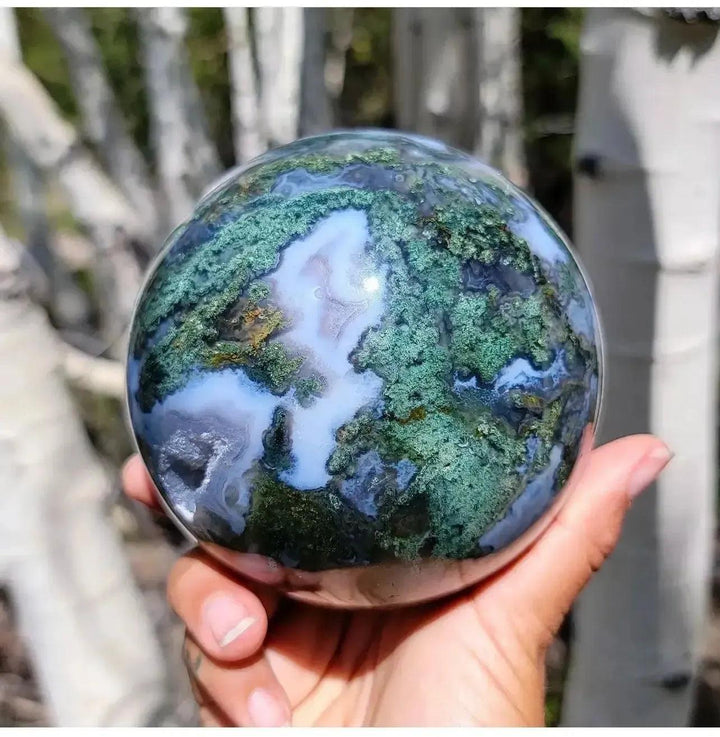 Hand holding a polished Moss Agate Crystal Sphere with green moss-like inclusions and white quartz, from Crystal Destiny.