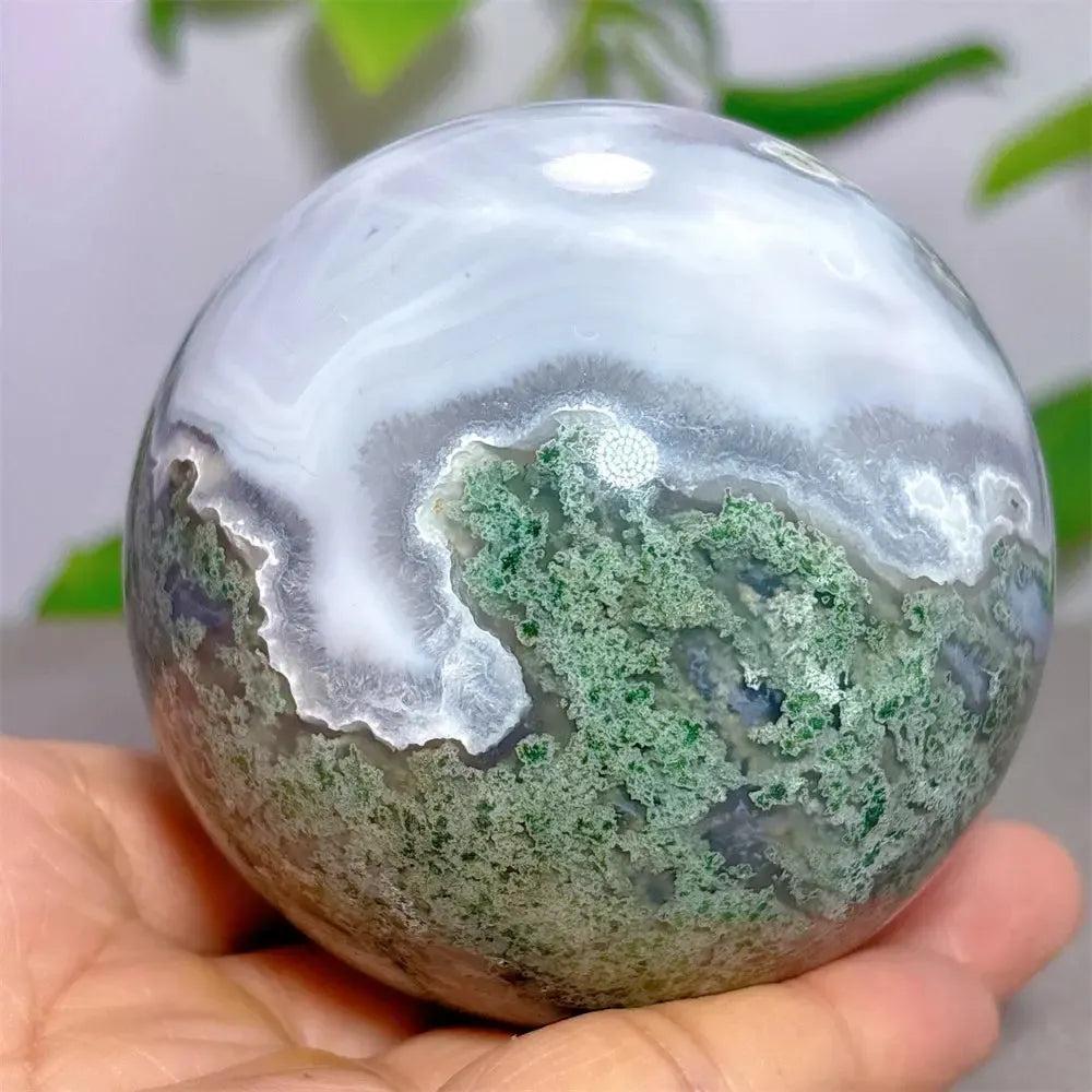 Polished Moss Agate sphere with vibrant green dendritic inclusions and white chalcedony, held in a hand by Crystal Destiny.