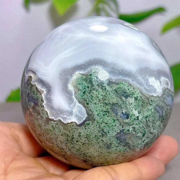 Polished Moss Agate sphere with vibrant green dendritic inclusions and white chalcedony, held in a hand by Crystal Destiny.