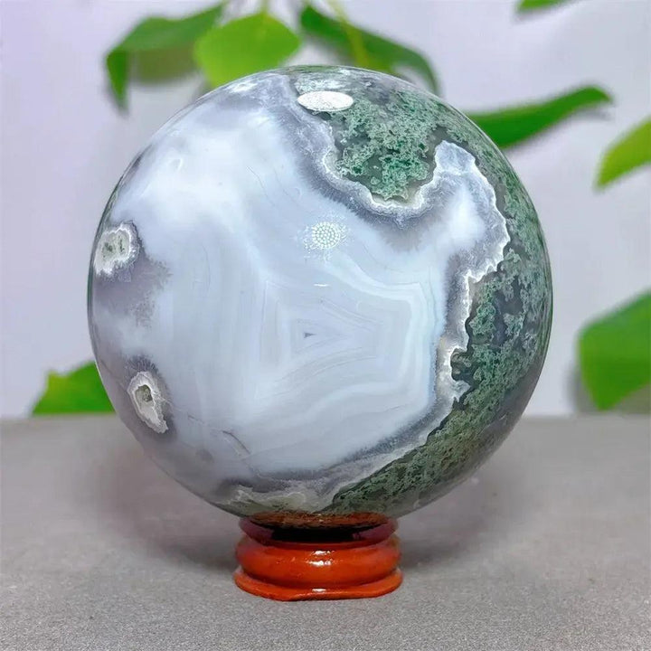 Moss Agate sphere from Crystal Destiny, featuring vibrant green and white dendritic patterns on a wooden stand.
