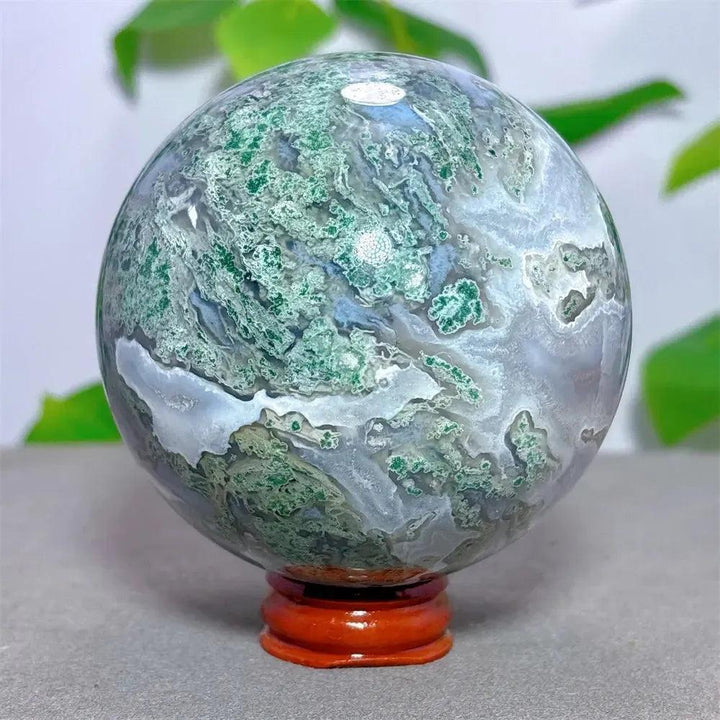 Moss Agate sphere from Crystal Destiny, featuring vibrant green dendritic inclusions and white chalcedony on a wooden stand.