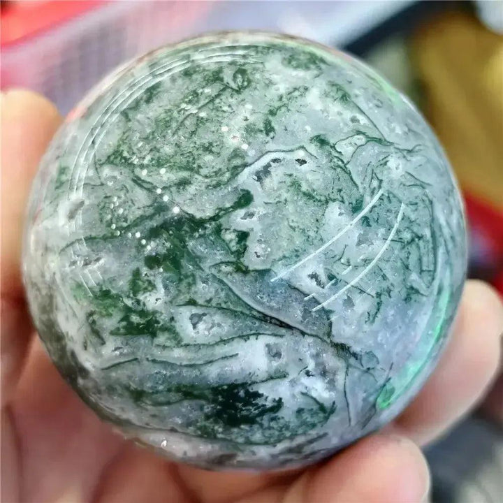 Hand-polished Moss Agate sphere from Crystal Destiny, featuring green dendritic inclusions and a smooth, reflective surface.